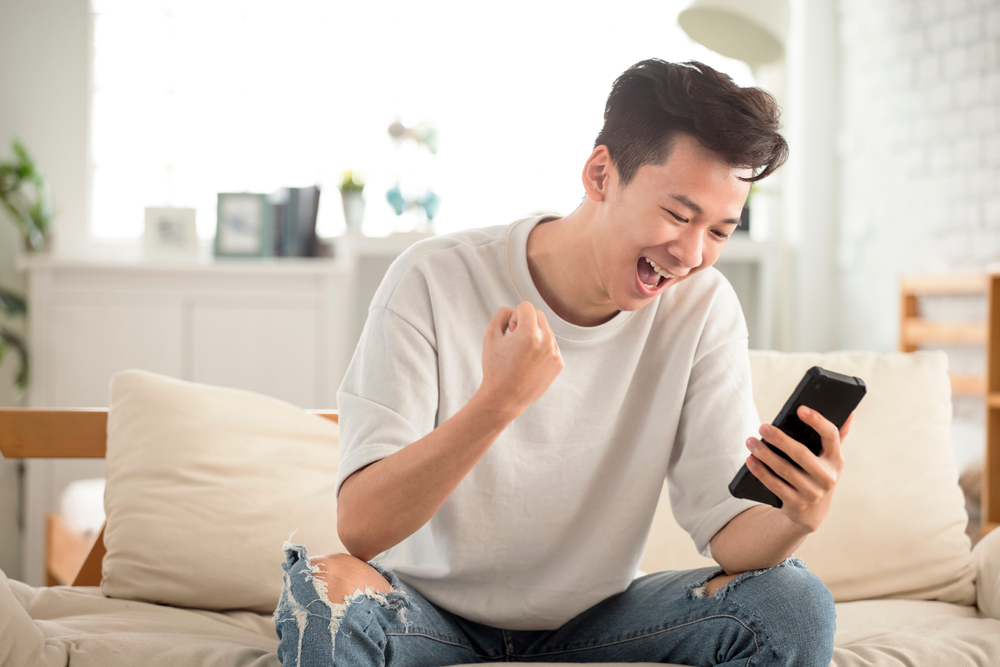 Happy,Young,Man,Looking,At,Cell,Phone,Celebrate,Receiving,Good